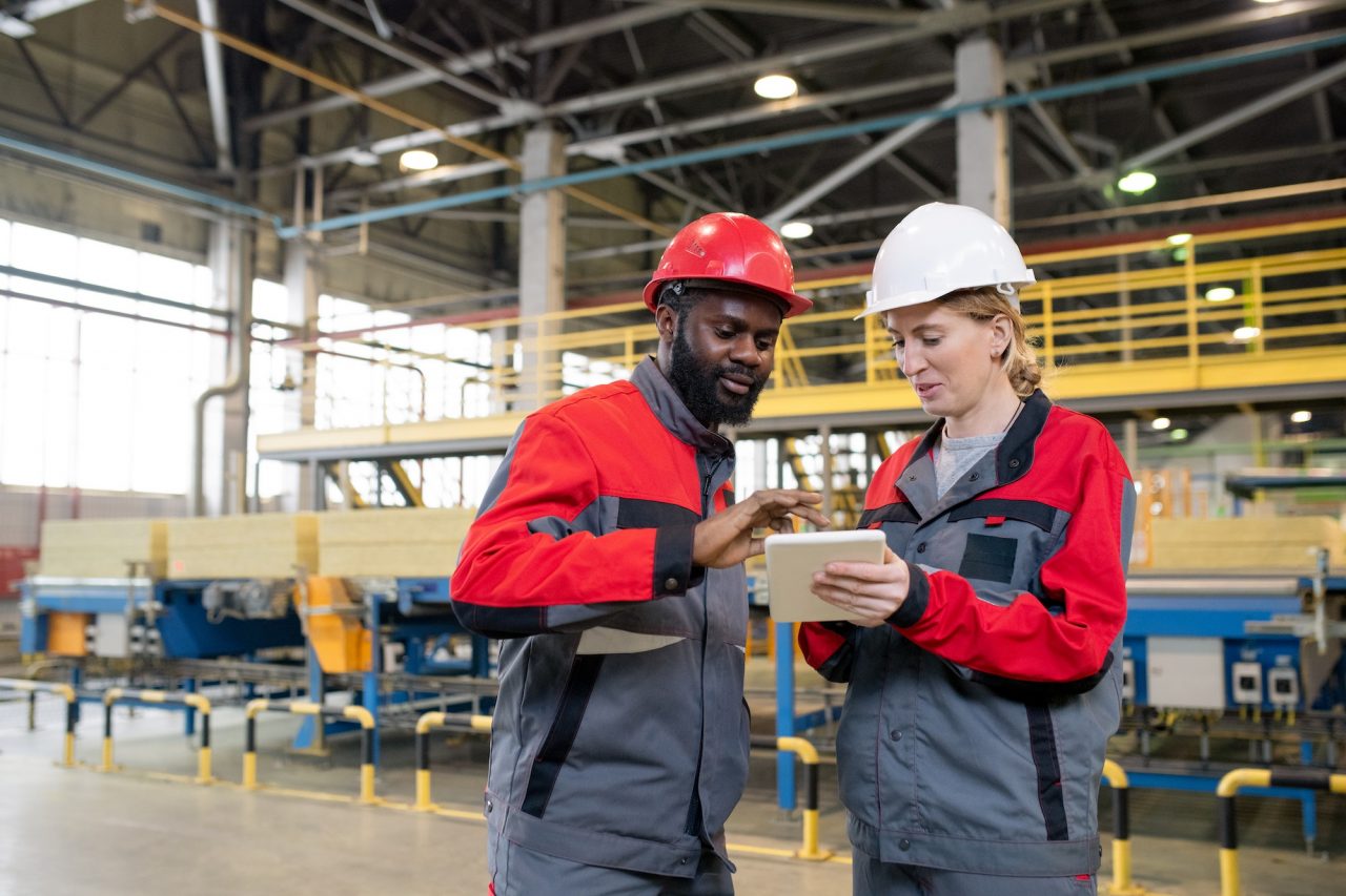 Ungoti Heat Treatment workers in protective gear reviewing production details on a digital tablet inside an industrial facility.